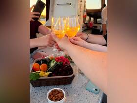 A group toasts with cocktails while enjoying a vibrant fruit platter aboard a boat, capturing the essence of celebration during a sunset cruise.