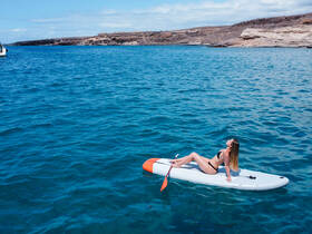 A woman enjoys a sunny day paddleboarding in crystal-clear waters, perfect for relaxation and water activities under the sun.