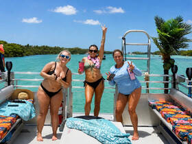 Three friends celebrate on a pontoon boat, enjoying drinks and the beautiful turquoise waters — a perfect day for fun in the sun.