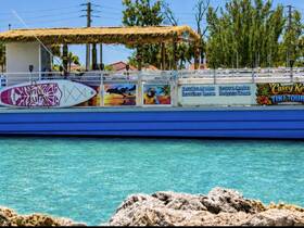 A vibrant tiki boat is docked, showcasing its colorful design and paddleboard, perfect for sunset cruises and dolphin tours.
