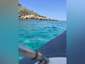 An unclear view of turquoise waters and rocky shoreline, with the boat's edge partially visible. The image lacks focus and clarity.