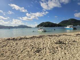 A vibrant beach scene featuring several boats anchored nearby, with people enjoying the water — a perfect setting for a day of relaxation and fun in the sun.