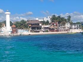 A picturesque view of a beachside resort with a lighthouse, surrounded by palm trees and clear turquoise waters, perfect for vacation getaways.