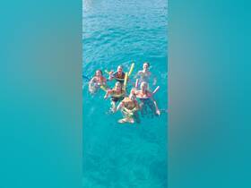 A lively group of friends enjoys a refreshing swim in crystal-clear waters, celebrating with cocktails and pool noodles — a perfect day of fun in the sun.