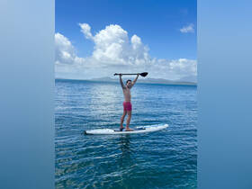 A young boy joyfully paddleboards in clear waters, showcasing the fun of outdoor water activities — perfect for family adventures.