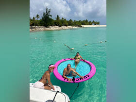 A lively group enjoys a sunny day in the turquoise waters, relaxing on a floating mat — perfect for beach fun and memorable summer adventures.