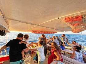 A lively group of guests celebrates aboard a boat, enjoying drinks and each other's company while taking in the beautiful ocean views — perfect for family gatherings or festive outings.