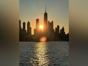 A stunning sunset casts a golden glow over the Chicago skyline, with shimmering reflections on the water — a perfect backdrop for evening boat cruises.
