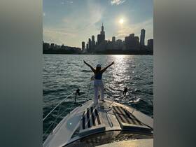 A woman celebrates on the bow of a boat against the stunning Chicago skyline at sunset, capturing the essence of urban boating adventures.