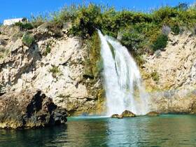 A stunning waterfall cascades down rocky cliffs into clear waters, showcasing the natural beauty of the coastline — a perfect spot for sightseeing during boat tours.