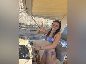 A young woman smiles and gives a thumbs up while at the helm of a boat, showcasing a fun and adventurous day on the water.