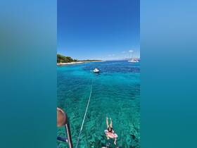 A child swims in the crystal-clear waters near an island, with a small boat in the background — a perfect summer day on the water.