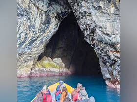 A group of adventurers explores a stunning cave entrance by boat, surrounded by dramatic rock formations and vibrant blue waters — a perfect setting for exploration and discovery.