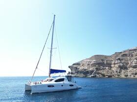 A sleek catamaran sails gracefully through clear waters, showcasing its elegant design against a stunning coastal backdrop.