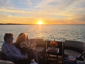 A couple enjoys a romantic sunset cruise on a pontoon boat, capturing the beautiful view as the sun sets over the water.