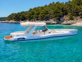 A sleek speedboat glides through crystal-clear turquoise waters, showcasing its elegant design against a backdrop of lush greenery and rocky coastline.