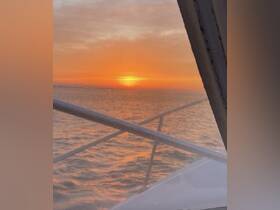 A stunning sunset view from the deck of a boat, showcasing vibrant orange hues reflecting on the water — perfect for romantic evenings or peaceful retreats on the sea.