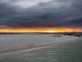 A stunning sunset view with a couple standing on a sandy beach, creating a romantic atmosphere perfect for memorable moments by the water.