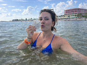 A woman enjoys a playful moment in the water, holding a sand dollar and posing for the camera — a perfect snapshot of beach fun and exploration.