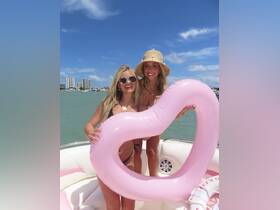 Two friends pose with a pink heart-shaped float on a sunny day aboard a boat, capturing the essence of summer fun and celebration on the water.