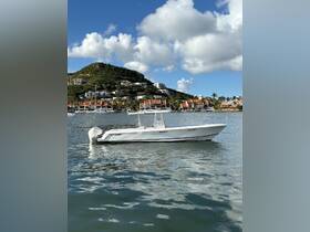 A sleek speedboat glides through calm waters, showcasing its elegant design against a picturesque backdrop of hillside homes and blue skies.