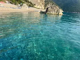 A serene view of clear waters and a rocky shoreline, showcasing the natural beauty of the coastline.