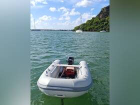 A clear view of a small inflatable boat with an outboard motor, anchored in calm waters, surrounded by sailboats and lush greenery — ideal for exploring coastal areas.