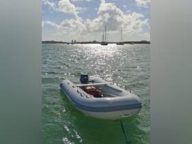 An inflatable boat is anchored in shimmering waters, with a backdrop of sailboats and a sunny sky, perfect for exploring coastal areas.