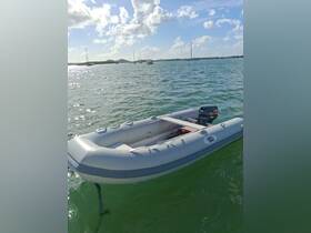 A sleek speedboat is anchored in clear waters, showcasing its design against a backdrop of distant sailboats and a sunny sky — perfect for exploring coastal destinations.