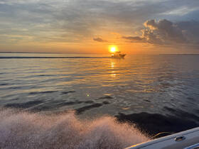 A stunning sunset over calm waters with a boat cruising in the distance, creating a picturesque scene perfect for evening boat trips.