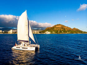 A stunning aerial view of a catamaran sailing on vibrant blue waters, with a picturesque mountain backdrop — perfect for showcasing sailing adventures in scenic locations.