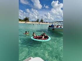 A lively group enjoys a sunny day on a floating mat in crystal-clear waters, perfect for beach fun and relaxation.