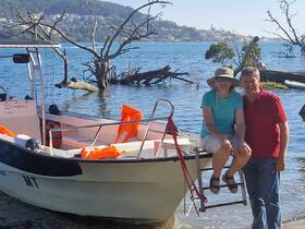 A cheerful couple poses on the steps of their boat, enjoying a sunny day by the water — perfect for romantic getaways or family adventures.