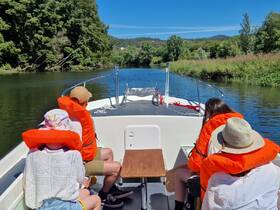 A group of friends enjoys a sunny day on a riverboat, wearing life jackets as they navigate through lush greenery — perfect for a relaxing day on the water.