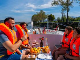 A joyful family enjoys a scenic boat ride, sharing food and drinks while wearing life jackets — perfect for a fun day on the water.