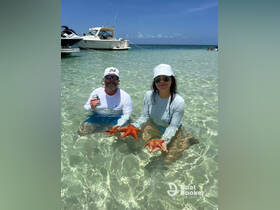 Two individuals enjoy a close encounter with starfish in shallow waters, showcasing the beauty of marine life during their aquatic adventure.