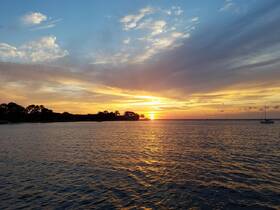 A stunning sunset over calm waters, with a sailboat silhouetted against the vibrant sky — a perfect backdrop for evening cruises or romantic getaways.