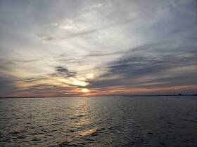 A serene sunset over calm waters, showcasing the beauty of nature and the coastline — perfect for peaceful evening boat rides.
