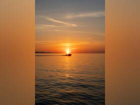A serene sunset view featuring a boat gliding across calm waters, creating a picturesque scene perfect for evening cruises.