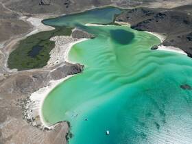 A stunning aerial view of a vibrant turquoise bay with boats anchored near a sandy beach, showcasing the natural beauty of the coastline and inviting exploration.