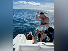 Two friends enjoy a fun moment on a boat, with one preparing to jump into the ocean while the other climbs aboard — a perfect snapshot of summer adventures on the water.