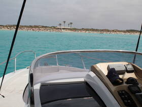 A view of the helm and console of a boat, showcasing the sleek design and equipment, with a beautiful turquoise water backdrop and a beach in the distance.