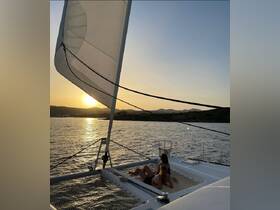 Two friends relax on the deck of a catamaran, enjoying a stunning sunset over the water — a perfect moment for sailing enthusiasts and sunset lovers.