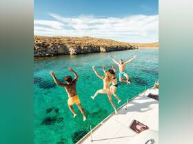A lively group of friends jumps into the crystal-clear waters from their boat, capturing the essence of summer fun and adventure on the water.
