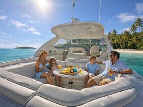 A joyful family enjoys drinks and snacks on a luxurious boat, surrounded by stunning turquoise waters and a picturesque beach backdrop — perfect for memorable family outings.