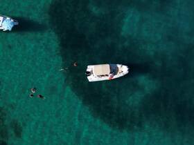 Aerial view of a group enjoying snorkeling in crystal-clear waters, with a boat anchored nearby — perfect for aquatic adventures and fun in the sun.
