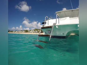 A close-up view of a boat's stern and ladder, set against a backdrop of clear turquoise waters and a sandy beach, ideal for a relaxing day on the water.
