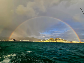 A stunning rainbow arcs over the coastline, creating a picturesque backdrop against the vibrant waters — a perfect scene for boat tours and scenic cruises.