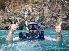 A snorkeler gives a thumbs up while enjoying the clear waters near a rocky coastline, capturing the excitement of underwater adventures.