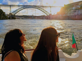 Two women enjoy a scenic sunset view from a boat on the river, with a stunning bridge in the background — a perfect moment for relaxation and sightseeing.